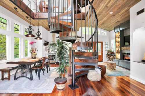 A modern interior featuring a spiral staircase, dining area, and large windows with natural light and greenery outside.
