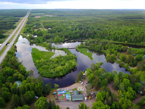 Aerial view of a lush green landscape with a winding river, surrounded by trees and a small building near the water.