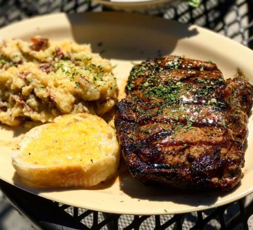 A plate featuring a grilled steak, creamy mashed potatoes, and a slice of garlic bread, garnished with herbs.