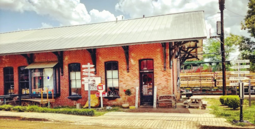 Historic brick building with a metal roof, featuring colorful signs and a charming outdoor seating area.