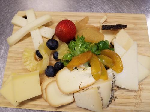 A wooden platter with assorted cheeses, fruits like strawberries and blueberries, and greens arranged artfully.