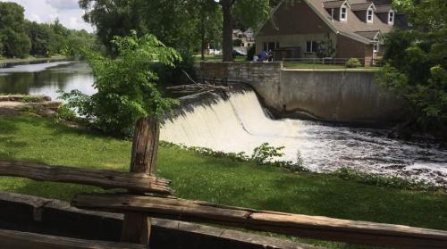 A serene scene of a waterfall flowing over a dam, surrounded by greenery and a residential area in the background.