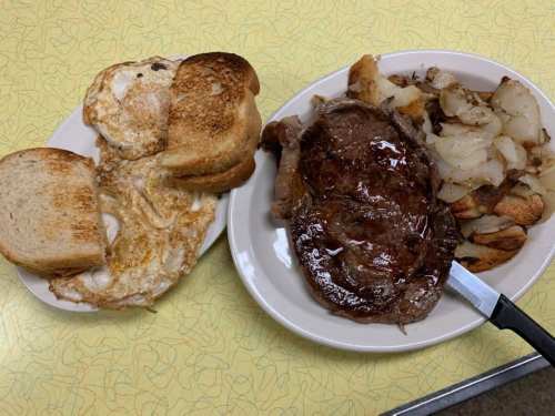A plate with a cooked steak, fried potatoes, and a side of toasted bread with an egg.