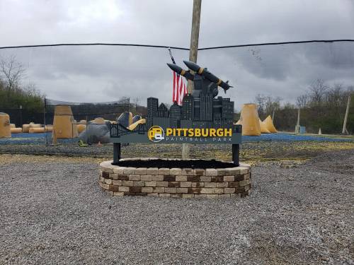 Sign for Pittsburgh Paintball Park featuring a city skyline and a missile, set against a cloudy sky.