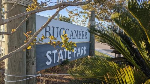 Sign for Buccaneer State Park surrounded by greenery and trees, with a clear blue sky in the background.