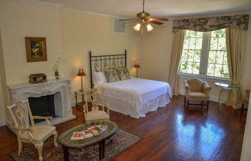 Cozy bedroom with a white bed, elegant chairs, a fireplace, and large windows letting in natural light.