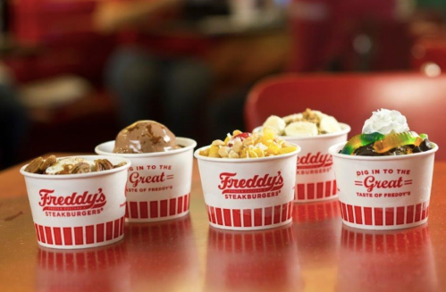 Five dessert cups from Freddy's Steakburgers, featuring various ice cream flavors and toppings, on a red table.