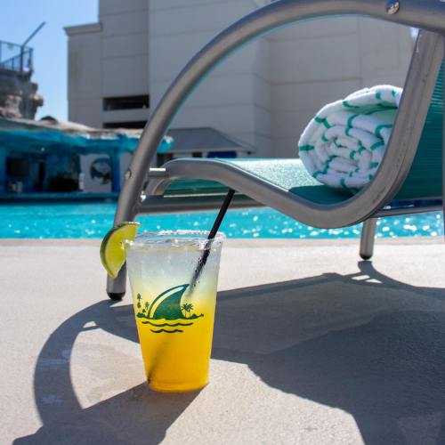 A refreshing drink with a lime slice sits beside a pool chair, with a towel rolled up in the background.