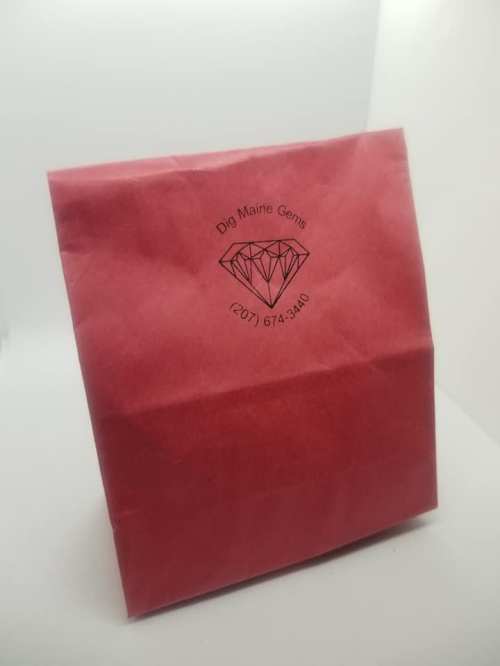 A pink paper bag with a logo featuring a diamond and the text "Dig Maine Gems" and a phone number.