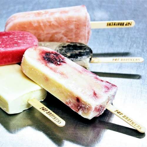 A variety of colorful frozen pops on sticks, featuring different flavors and textures, arranged on a metallic surface.