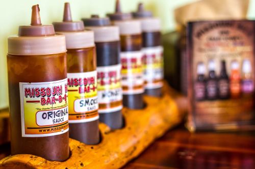 A wooden holder with various bottles of barbecue sauce labeled "Missouri Bar-B-Q" in a restaurant setting.