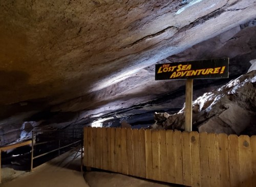 Sign for "The Lost Sea Adventure" inside a cave, with rocky walls and a wooden fence in the foreground.