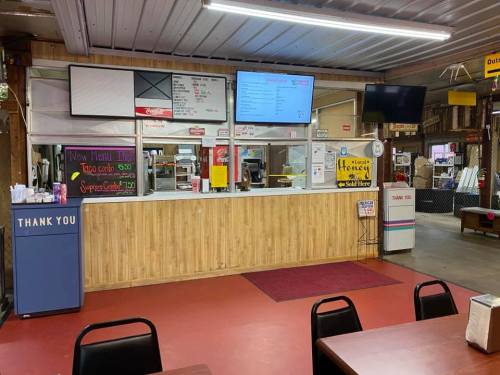 Interior of a casual eatery with a service counter, menu board, and seating area. Warm wooden decor and red flooring.