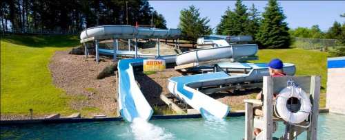 A water park with multiple blue water slides and a lifeguard on duty overlooking the pool area.