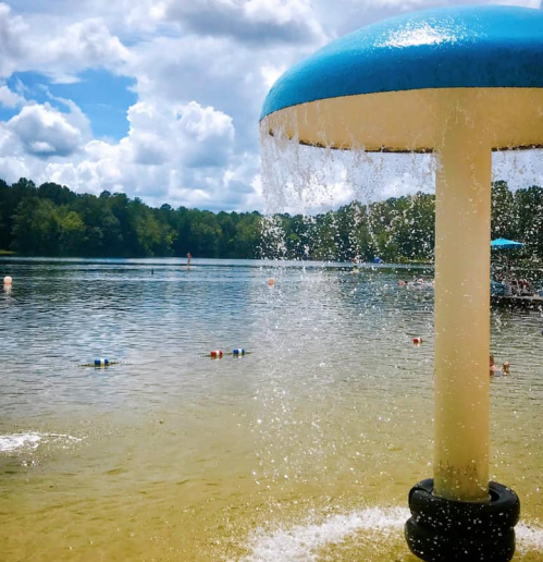A water feature with a blue top sprays water into a calm lake under a partly cloudy sky.