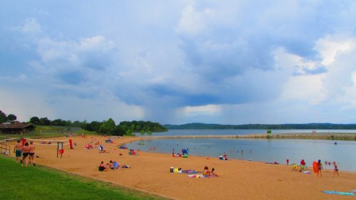 A sandy beach with people sunbathing and swimming, under a cloudy sky with distant rain.