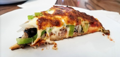 A slice of pizza topped with melted cheese, green peppers, onions, and black olives on a white plate.