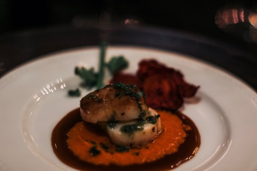 A plated dish featuring seared fish on a bed of orange sauce, garnished with herbs and accompanied by crispy vegetables.