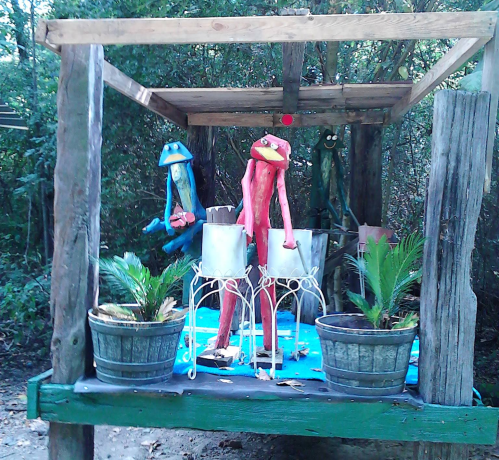 Colorful wooden sculptures of frogs and other characters on a rustic wooden structure with potted plants.