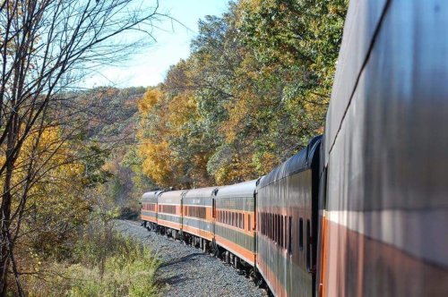 A vintage train travels along a winding track surrounded by colorful autumn trees.
