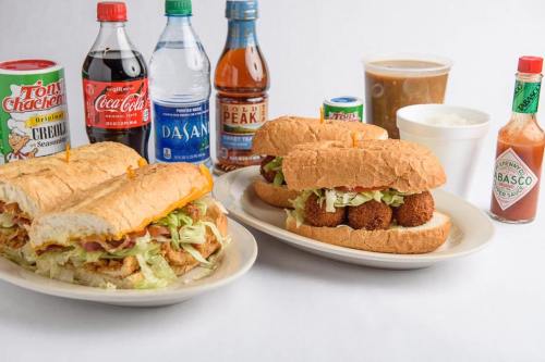 Two plates of sandwiches filled with lettuce and fried items, surrounded by various drinks and condiments.