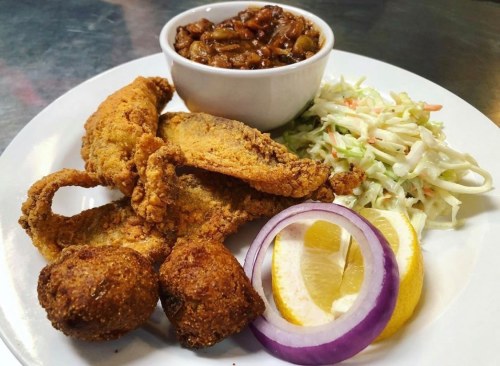 A plate of fried catfish, coleslaw, baked beans, and lemon slices, garnished with red onion.