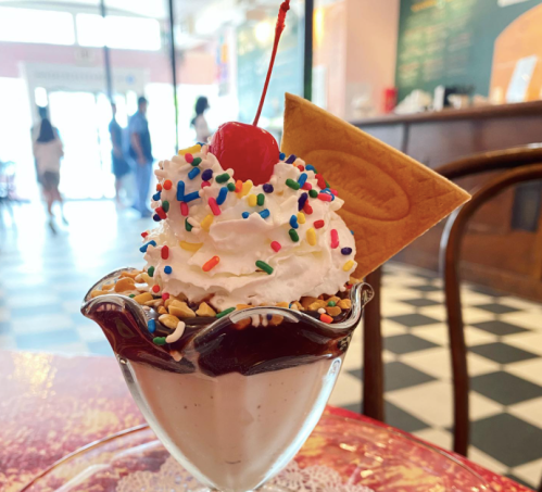A delicious ice cream sundae topped with whipped cream, a cherry, sprinkles, and a cookie, served in a glass dish.