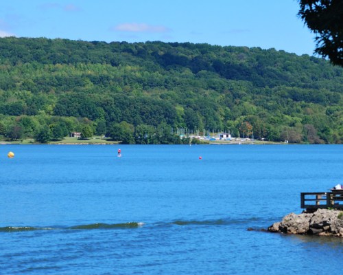 A serene lake scene with blue water, green hills in the background, and a few boats moored near the shore.