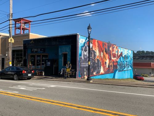A colorful mural on a building exterior, depicting a train scene, with outdoor seating and a street view.