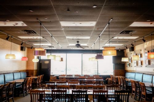 Interior of a restaurant with wooden tables, chairs, and colorful pendant lights hanging from the ceiling.