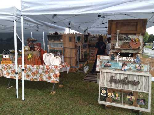 A craft fair booth with handmade items, including wooden signs and decorations, under a white canopy.