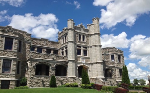 A large stone castle with turrets, surrounded by green grass and blue skies with fluffy clouds.