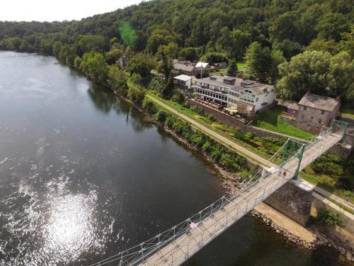 Aerial view of a suspension bridge over a river, with lush greenery and buildings along the shore.