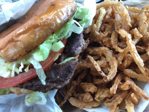 A close-up of a burger with lettuce and tomato, served with a side of crispy fried onions.