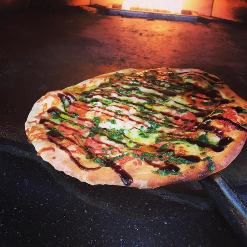 A freshly baked pizza with toppings, resting on a stone surface near a glowing oven.