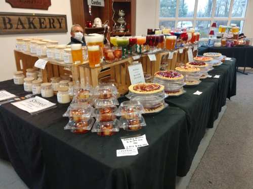 A display of various baked goods and candles on tables, featuring pies, jars, and colorful drinks in a cozy setting.