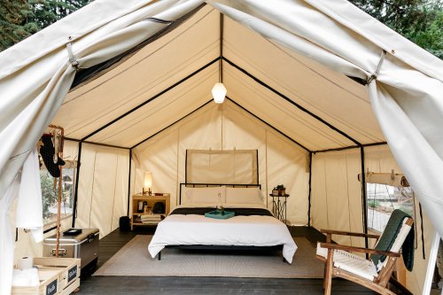 Cozy glamping tent interior with a bed, side tables, and a chair, surrounded by natural light and rustic decor.