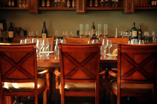 A wooden dining table set with glasses and wine bottles, featuring three empty chairs in a cozy restaurant setting.