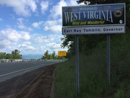 Welcome sign for West Virginia, featuring "Wild and Wonderful" slogan, with a blue sky and green landscape in the background.