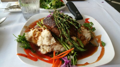 A plate of beef with herbs, served on mashed potatoes and asparagus, garnished with carrots and colorful herbs.
