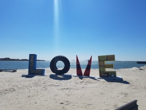 Colorful "LOVE" letters on a sandy beach with a clear blue sky and water in the background.