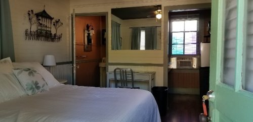 Cozy room with a bed, desk, and air conditioner, featuring light-colored walls and a window with colorful blinds.