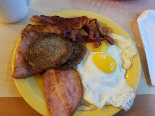 A yellow plate with a fried egg, bacon, and two sausage patties.