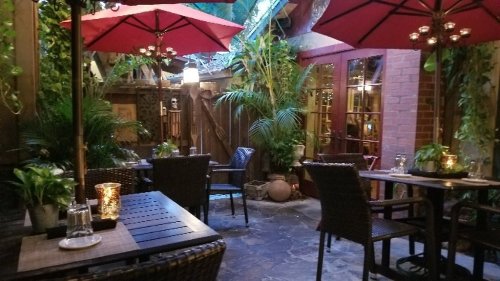 Cozy outdoor dining area with wicker chairs, red umbrellas, and lush greenery, creating a serene atmosphere.