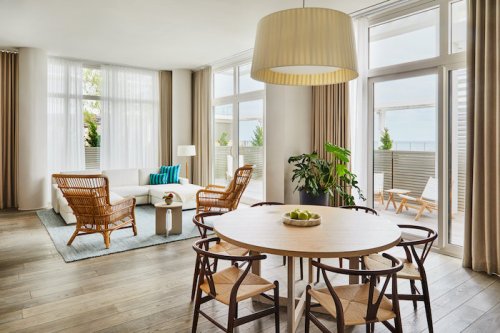 Bright, modern living space with large windows, a cozy seating area, and a dining table surrounded by chairs.