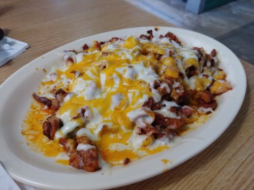 A plate of cheesy nachos topped with melted cheddar, diced meat, and drizzled with creamy sauce.