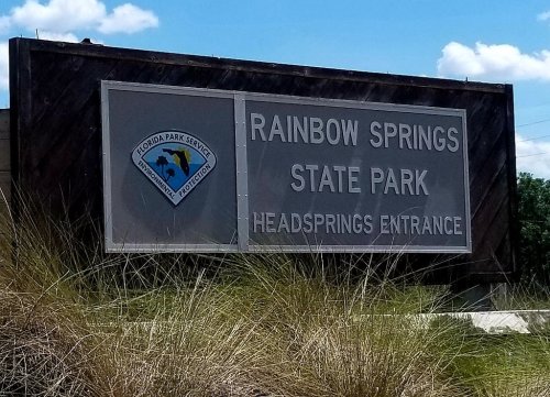 Sign for Rainbow Springs State Park, Headsprings Entrance, with blue sky and grass in the foreground.