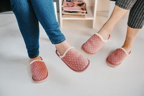 Two pairs of feet in cozy pink slippers with white polka dots, resting on a light floor.