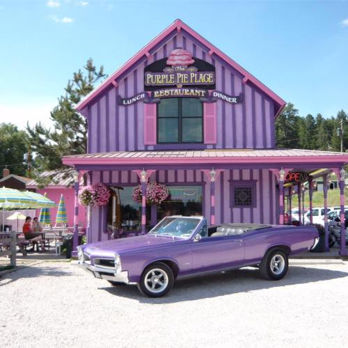 A purple convertible parked in front of a colorful restaurant called "The Purple Pie Place."