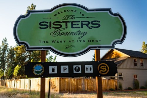 Welcome sign for Sisters Country, featuring icons for amenities like parking and restrooms.